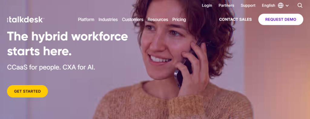 Talkdesk homepage with headline "The hybrid workforce starts here. CCaaS for people. CXA for AI." — featuring a smiling woman talking on a phone against a warm purple-toned background
